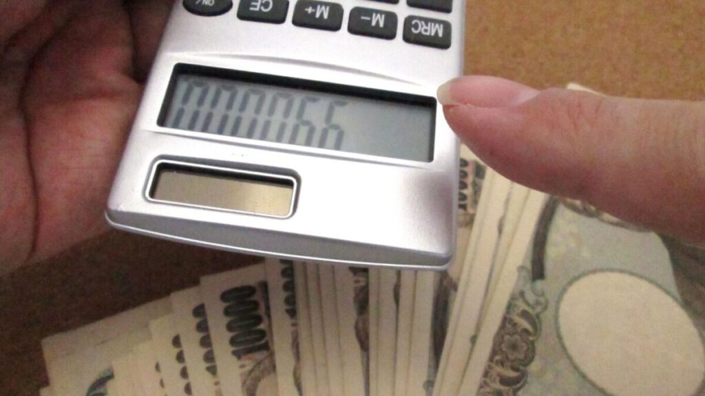 一万円札と電卓で金額を打ち込んでいる画像