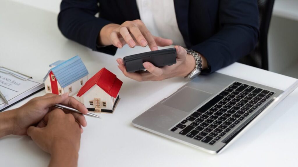 パソコンと模型の家、担当営業が電卓計算している画像